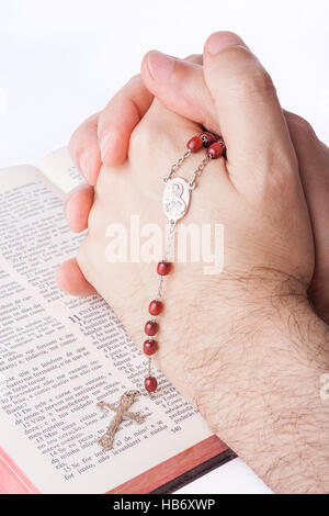 Male hands closed in prayer holding a rosary over an open old Holy Bible. Stock Photo