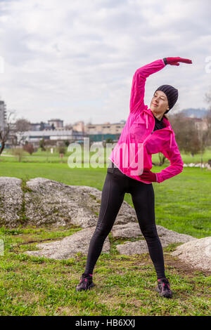 Young woman warming up and stretching the upper body and arms before running on a cold winter day in a park. Stock Photo