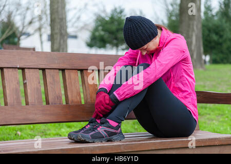 Young athlete woman tired or depressed resting on a bench on a cold winter day in the track of an urban park. Stock Photo