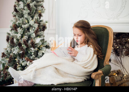 Little girl reading book near Christmas tree Stock Photo