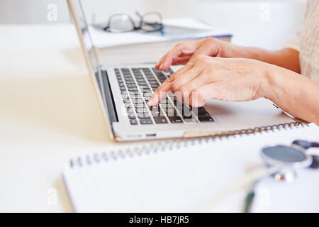 Doctor writing on laptop computer report on patient record Stock Photo