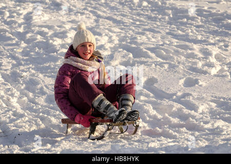 Active young cute girl sledding down the hill on sunny winter day Stock Photo