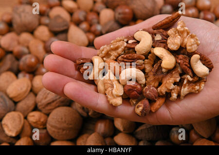 General view of mixed nuts, including cashew, almonds, hazlenuts, walnuts, pecan nuts and pistachio nuts being held in a hand and in their shells hazelnuts, walnuts, almonds, and Brazil nuts. Stock Photo