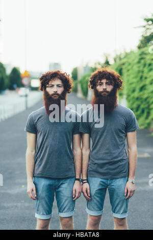 Portrait of identical adult male twins with red hair and beards on sidewalk Stock Photo