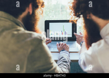 Over shoulder view of male twins working on laptop in office Stock Photo