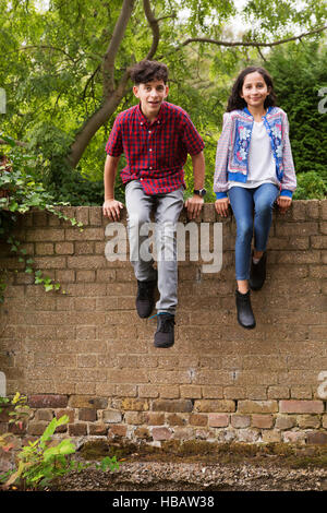 Portrait of brother and sister sitting on wall Stock Photo