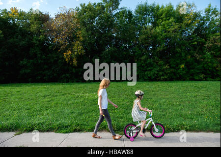 Young girl riding her bicycle followed by mother Stock Photo