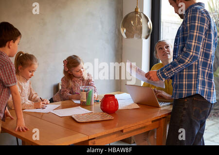 Couple having discussion at dining table whilst son and daughters colouring Stock Photo