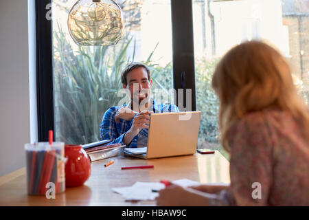 Mid adult man using laptop at dining table whilst daughter colouring Stock Photo