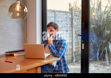 Mid adult man reading laptop update at dining table Stock Photo