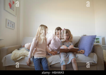 Mid adult woman and daughters reading storybook on sofa Stock Photo