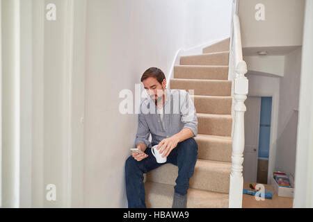 Mid adult man sitting on staircase reading smartphone texts Stock Photo