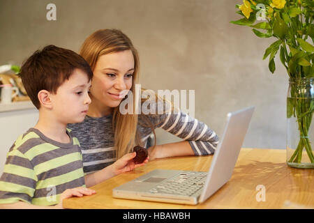 Mid adult woman and son looking at laptop on dining table Stock Photo