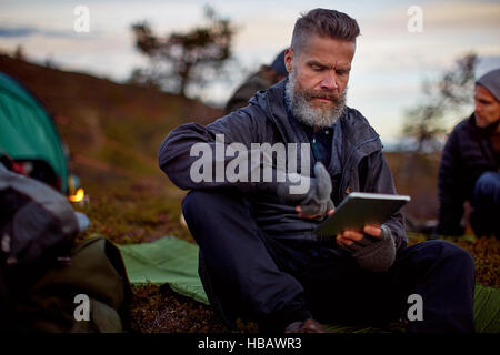Hiker using digital tablet by tent, Keimiotunturi, Lapland, Finland Stock Photo