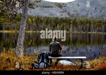 Hiker resting on bench, looking out at lake, Kesankijarvi, Lapland, Finland Stock Photo