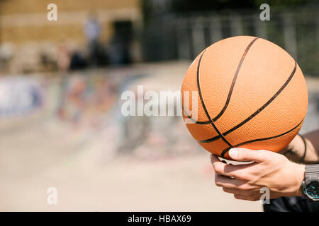 Young mans hands holding basketball ball in city skatepark Stock Photo