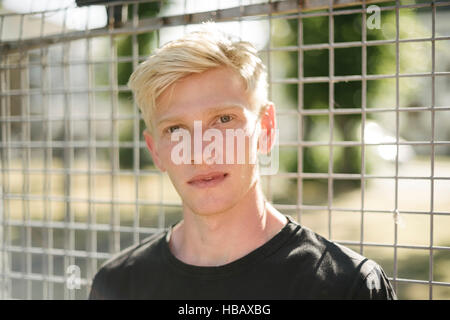Portrait of blond haired young man by wire fence Stock Photo