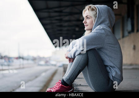 Portrait of mid adult female runner in grey hoody, sitting gazing Stock Photo