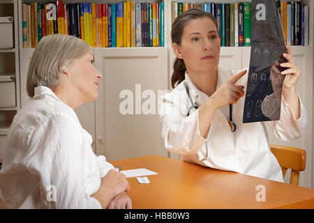 Experienced doctor in white coat showing her female patient on an image of ct-scans of her brain where the tumor is located Stock Photo