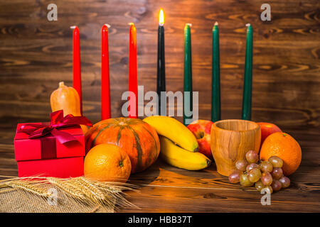 african Kwanzaa festive concept with decorative candles red, black and green, gift box, pumpkins, ears of wheat, grapes, orange, banana, bowl and frui Stock Photo