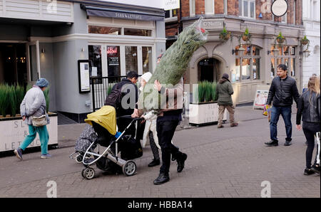 Man with his family carrying a newly bought real Christmas tree in Sutton Surrey UK
