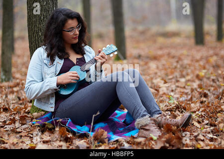 Hispanic young girl playing ukulele outdoor in the forest Stock Photo
