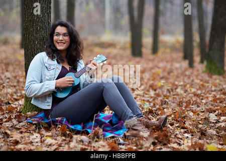 Hispanic young girl playing ukulele outdoor in the forest Stock Photo