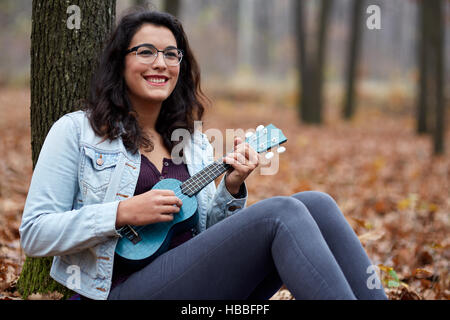 Hispanic young girl playing ukulele outdoor in the forest Stock Photo