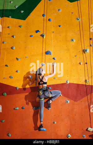 Pretty woman climbing up the orange wall in gym Stock Photo