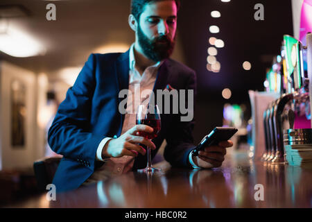 Businessman using mobile phone with glass of red wine in hand Stock Photo