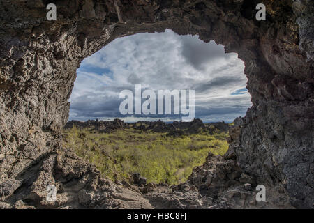 A round natural window in the volcanic rocks overlooking lava field covered by the vegetation. Stock Photo