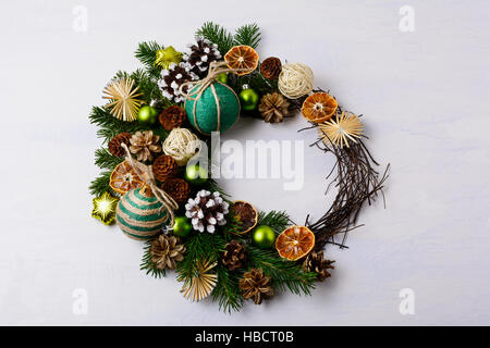Christmas wreath with snowy pine cones and rustic ornaments. Christmas decoration with fir branches, green balls, homemade twine and straw stars. Stock Photo