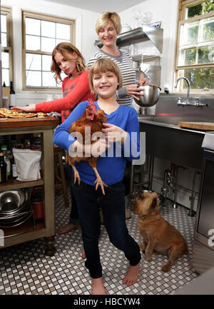 Mother and daughters in kitchen preparing folder, younger daughter holding pet chicken Stock Photo