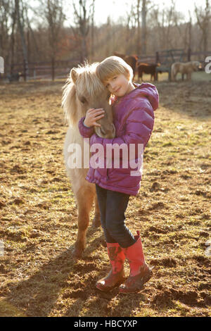 Portrait of young girl outdoors, hugging pony Stock Photo