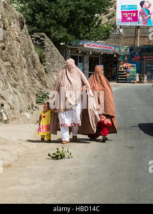 Two women wearing burkhas and a child walking along a road in northern Pakistan Stock Photo
