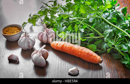 On the table are the vegetables for cooking: parsley leaves, carrots , garlic and spices. Stock Photo