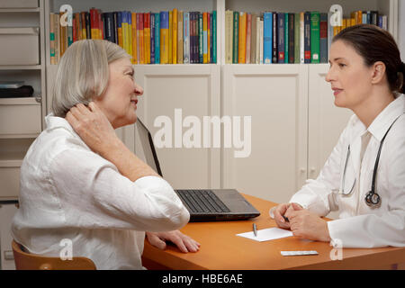 Senior female patient consulting middle aged doctor because of strong neck pain caused by muscular tension Stock Photo
