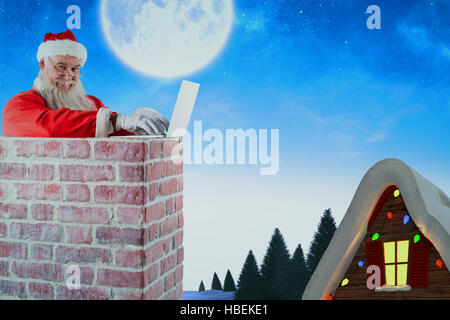 Composite image of santa claus using laptop on chimney Stock Photo