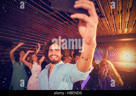 Composite image of man taking a selfie from mobile phone while friends dancing on dance floor Stock Photo