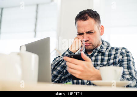 Tired handsome young freelancer is using a mobile phone while working at the coffee shop Stock Photo