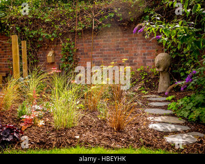 Stepping stone path through garden flower bed with bark chippings and brick wall Stock Photo