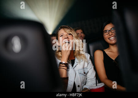 Smiling young women in cinema hall eating popcorn and watching movie Stock Photo