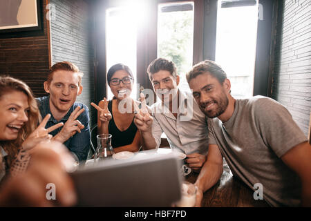 Multiracial people having fun at cafe taking a selfie with mobile phone. Group of young friends sitting  at restaurant taking self portrait with smart