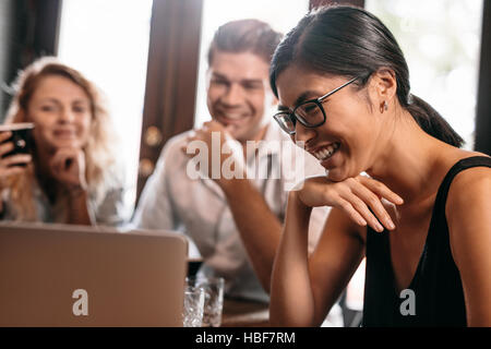 Close up shot of smiling asian woman looking at laptop with friends in cafe. Friends in coffee shop looking at laptop and smiling. Stock Photo
