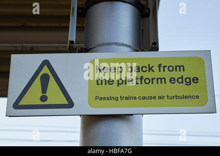 train station platform warning sign keep back from platform edge passing trains cause air turbulence Stock Photo