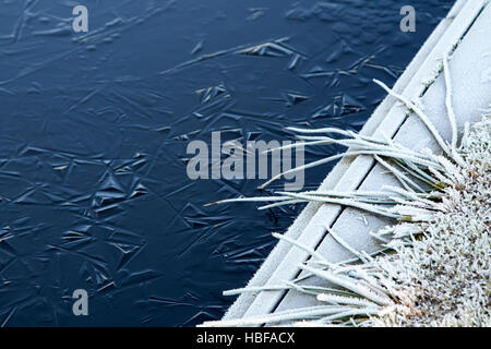frost on edge of frozen small lake pond on a cold winter morning in the uk Stock Photo