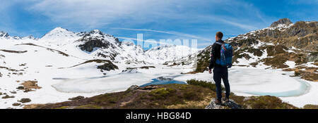 Young man, hiker looking at frozen lake, Unterer Giglachsee, mountain landscape with residual snow, Rohrmoos-Obertal Stock Photo