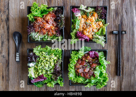 Top-down view of  4 Poke bowls with chopsticks and a spoon on a wooden surface. 3 fishes options and one vegetarian option. Stock Photo