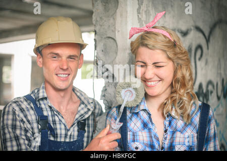 Portrait of a young man and woman in overalls with roller for painting in hands. Concept of construction and home repair. Stock Photo