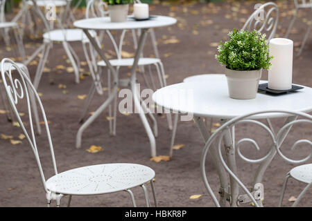Outdoor restaurant background interior, metal white chairs and tables with decorative green plants in pots and candles Stock Photo